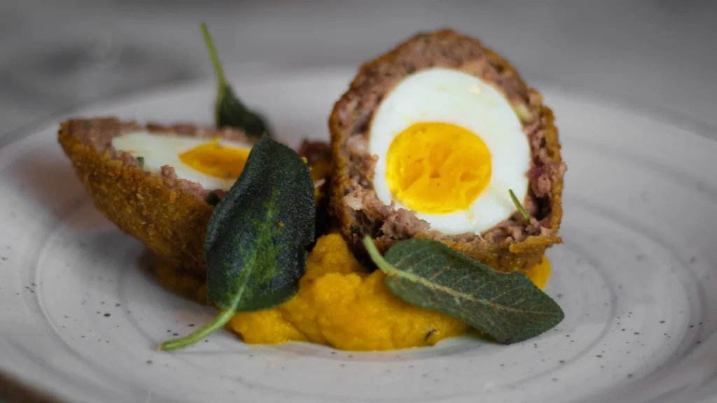 Scotch Eggs tagliate a metà su crema di zucca con salvia fritta